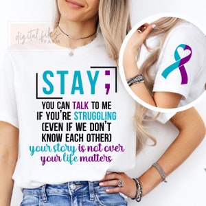 K&ouml;nnte beinhalten: Wei&szlig;es T-Shirt mit dem Text "STAY; YOU CAN TALK TO ME IF YOU'RE STRUGGLING (EVEN IF WE DON'T KNOW EACH OTHER) your story is not over your life matters". Das Shirt zeigt au&szlig;erdem ein t&uuml;rkisfarbenes und violettes Band mit einem Herz in der Mitte.
