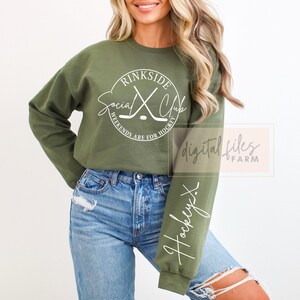 May include: A green sweatshirt with a white circle graphic that says "Rinkside Social Club" with hockey sticks crossed inside the circle. The text below the circle says "Weekends are for hockey". The sweatshirt has a white "Hockey" written on the sleeve.
