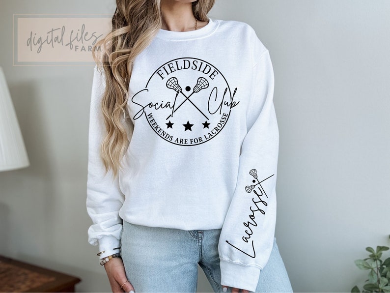 Może przedstawiać: Biała bluza z czarnym kołem z napisem "Fieldside Social Club" i skrzyżowanymi kijami do lacrosse. Pod kołem znajduje się napis "Weekends are for Lacrosse". Lewy rękaw ma czarny wz&oacute;r z kijami do lacrosse i napisem "Lacrosse" napisanym kursywą.