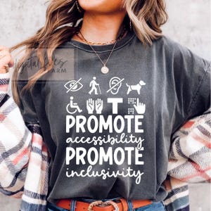 May include: Dark gray t-shirt with white text and accessibility symbols. The shirt reads "PROMOTE accessibility PROMOTE inclusivity." The design includes symbols for visual, mobility, and hearing impairments, and a service dog.