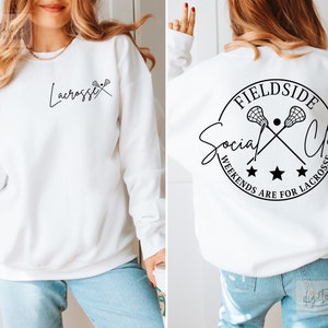 Może przedstawiać: Biała bluza z czarnym tekstem i grafiką kija do lacrosse. Prz&oacute;d głosi "Lacrosse", a tył "Fieldside Social Club Weekends Are For Lacrosse".