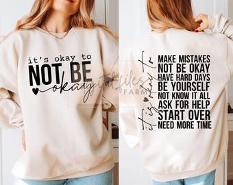 May include: A cream-colored sweatshirt with black text that reads "it's okay to NOT BE okay" on the front and "it's okay to MAKE MISTAKES NOT BE OKAY HAVE HARD DAYS BE YOURSELF NOT KNOW IT ALL ASK FOR HELP START OVER NEED MORE TIME" on the back.