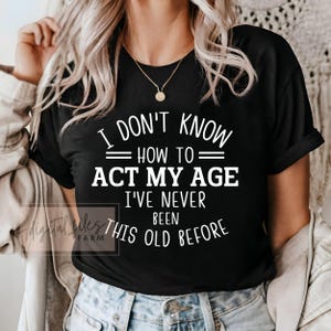 May include: Black t-shirt with white text that reads "I don't know how to act my age I've never been this old before".