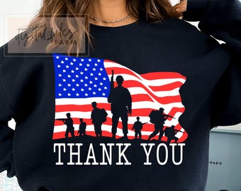 May include: Black sweatshirt featuring a graphic of the American flag with silhouettes of soldiers. The flag design includes red and white stripes and a blue field of stars. The words "THANK YOU" are printed in white.
