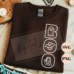 May include: A dark brown crewneck sweatshirt featuring a white graphic design with the word BOO. The letter B contains a ghost, the letter O contains a bat, and the second O contains a cat sitting on a pumpkin. The text SVG and PNG appear in circles.