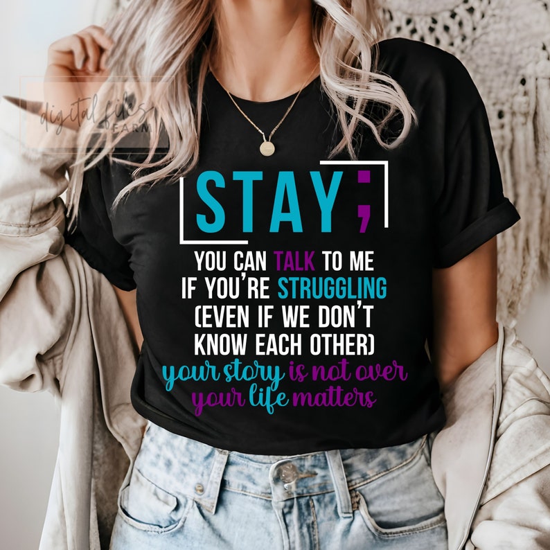 K&ouml;nnte beinhalten: Schwarzes T-Shirt mit dem Text "STAY; YOU CAN TALK TO ME IF YOU'RE STRUGGLING (EVEN IF WE DON'T KNOW EACH OTHER) your story is not over your life matters" in rosa, blau und lila.