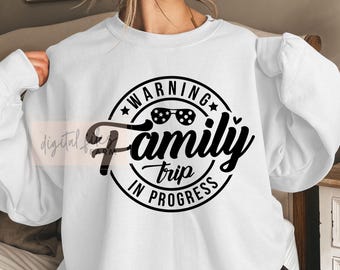 Può includere: Felpa bianca con grafica nera che recita "WARNING Family Trip In Progress". Il design include occhiali da sole e stelle. La felpa è in stile casual, adatta per viaggi o gite in famiglia.