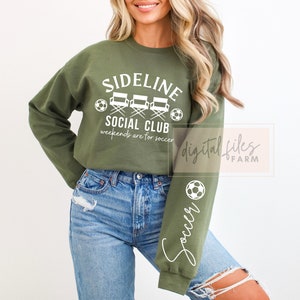 May include: A green sweatshirt with the text "Sideline Social Club" and "Weekends are for soccer" in white. The sweatshirt has a graphic of three director's chairs and a soccer ball. The right sleeve has the word "Soccer" written vertically in white.