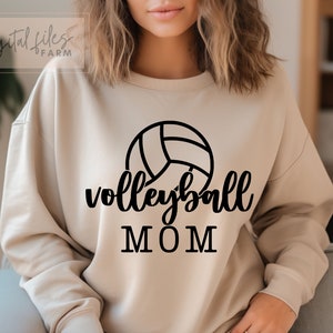 May include: A tan sweatshirt with a black volleyball graphic and the text "volleyball MOM" printed on the front.