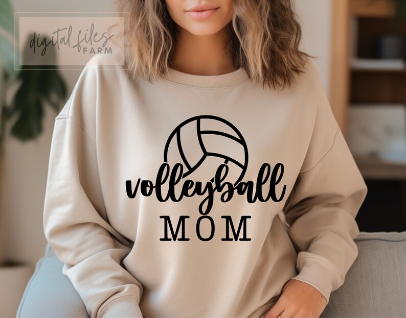 May include: A tan sweatshirt with a black volleyball graphic and the text "volleyball MOM" printed on the front.