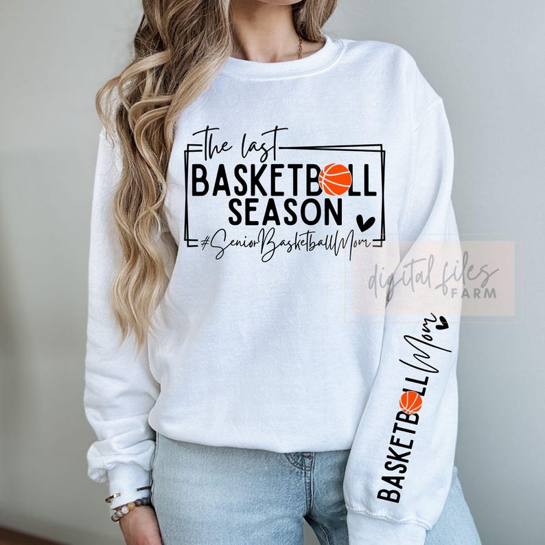 May include: White sweatshirt with black text that reads "The Last Basketball Season" with a basketball graphic and heart. The sleeve has the text "Basketball Mom" with a basketball graphic and heart.