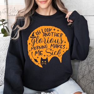 May include: Black sweatshirt with an orange graphic of a witch's hat, a crescent moon, and a black cat. The text on the graphic reads "Oh look another glorious morning makes me sick."