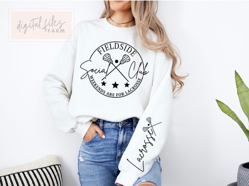 Może przedstawiać: Biała bluza z czarnym kołem graficznym, na kt&oacute;rym widnieje napis "Fieldside Social Club" z krzyżującymi się kijami do lacrosse i tekst "Weekends are for Lacrosse". Lewy rękaw ma napis "Lacrosse" napisany kursywą.