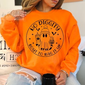Può includere: Felpa arancione con un grafico circolare nero che presenta un fantasma con un cappello e che tiene una zucca e una tazza. Il testo intorno al fantasma dice "No Diggity Bout To Bag It Up".