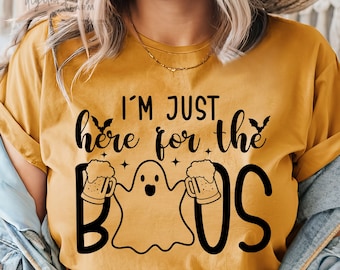 May include: A mustard yellow t-shirt with a black graphic of a ghost holding two mugs of beer. The text "I'm just here for the boos" is printed on the shirt.