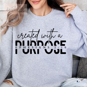 Puede incluir: Sudadera gris con el texto "created with a purpose" y "Ephesians 2:10" en negro.