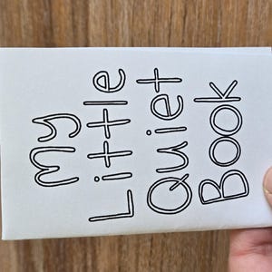 May include: A white rectangular booklet with the text "my little Quiet Book" printed in black outline font on the front cover. The cover features a simple, clean design with the title centered in a playful, rounded typeface on a plain white background.