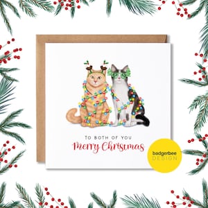 May include: A Christmas card featuring two cats wearing festive attire. One cat is wearing reindeer antlers and the other is wearing green glasses. Both cats are tangled in Christmas lights. The card reads "To both of you Merry Christmas" and "badgerbee DESIGN".
