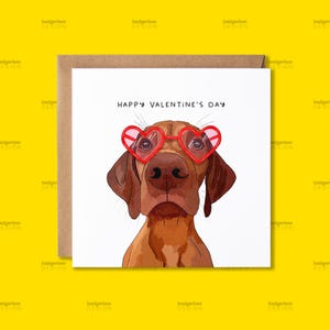 Op de afbeelding: Een Valentijnskaart met een bruine en witte hond die een rode hartvormige zonnebril draagt. De kaart heeft de tekst "Happy Valentine's Day" erop gedrukt.