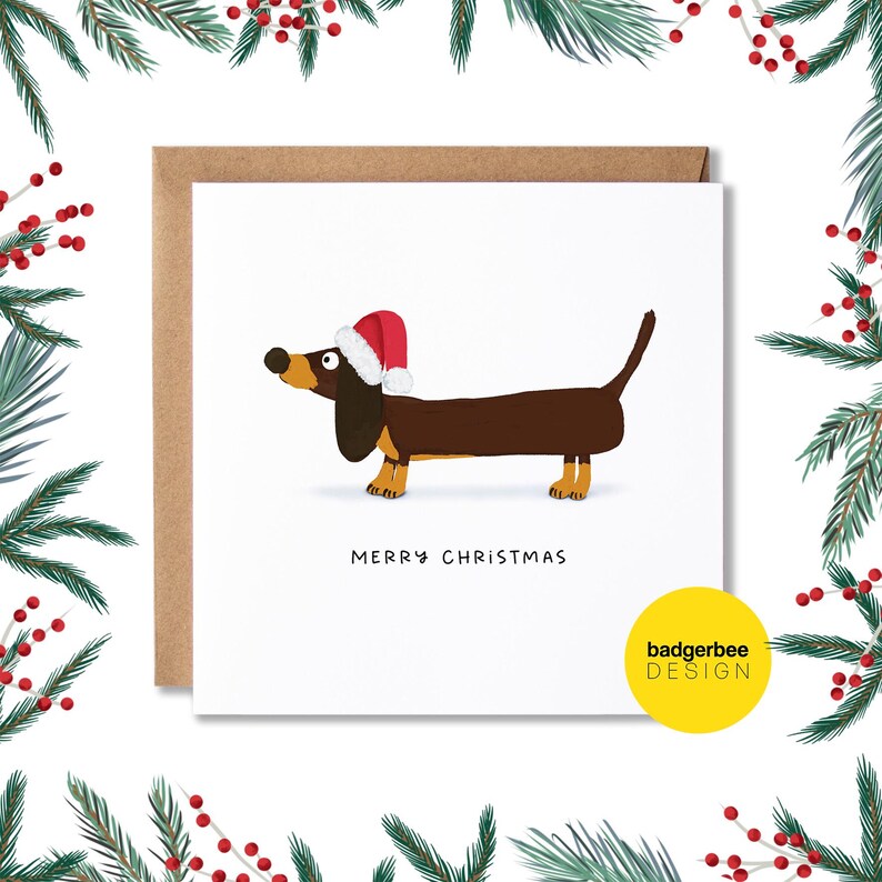 Pu&ograve; includere: Un biglietto di auguri di Natale con un bassotto di cartone animato che indossa un cappello di Babbo Natale. Il biglietto ha il testo "Buon Natale" e un piccolo logo che dice "badgerbee DESIGN".