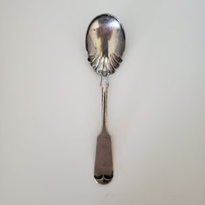 May include: A silver sugar spoon with a scalloped bowl and a simple, rounded handle.