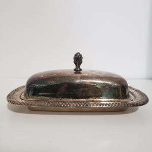May include: Silver butter dish with a domed lid and a decorative knob. The dish has a rope-like design around the edge.