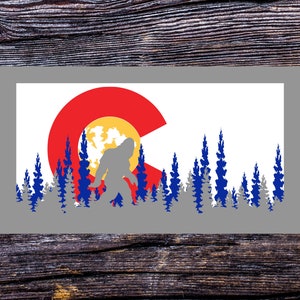 May include: A white background with a silhouette of Bigfoot standing in front of a stylised Colorado flag. The flag is red, yellow, and blue. The silhouette of Bigfoot is grey. The background is a grey rectangle.