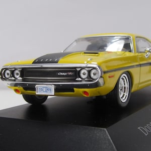 May include: A yellow 1970 Dodge Challenger R/T scale model car featuring a black hood stripe, black side stripes, chrome bumpers, and a front license plate that reads 32c 1935. The vehicle is mounted on a black display base with the text Dodge Challenger R/T 440 1970.