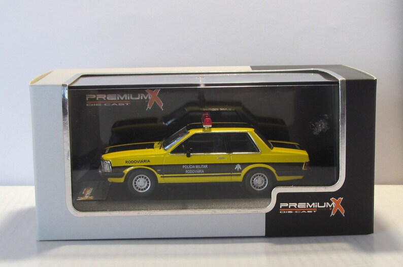 May include: A yellow and black diecast model car of a Brazilian police car. The car has a red light on top and the words "Policia Militar Rodoviaria" on the side. The car is in a clear plastic display case.