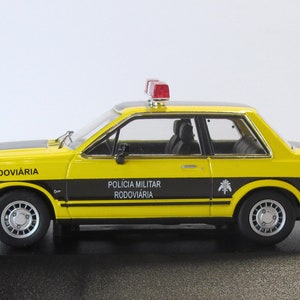 May include: Yellow and black diecast model car of a Ford Corcel, a Brazilian car, with a red light on top. The car is labeled "Pol&iacute;cia Militar Rodovi&aacute;ria" and "Rodovi&aacute;ria".