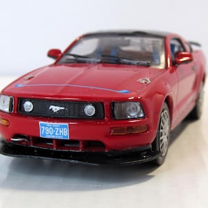 May include: Red Ford Mustang toy car with a black roof and a New Jersey license plate that reads "790-ZHB".