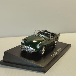 Puede incluir: Un coche modelo Daimler SP250 verde oscuro sobre una base negra. El coche en miniatura tiene una capota descapotable, adornos plateados y ruedas detalladas. La base tiene el nombre del coche impreso.