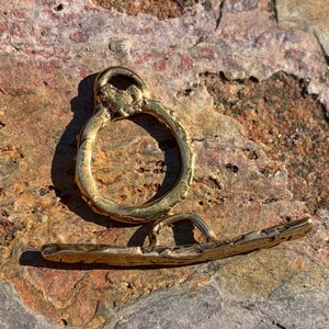 May include: Two gold-toned metal clasps, one is a round ring with a small loop on top, the other is a flat bar with a loop on one end.