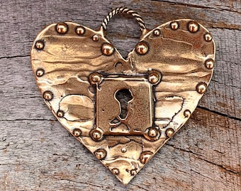 May include: A heart-shaped pendant made of brass with a keyhole design. The pendant has a textured surface and is decorated with small, round studs.