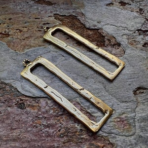 May include: Two gold-toned metal rectangular frames with a textured surface. The frames have a small loop at the top for hanging.