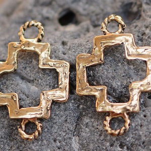May include: Two gold-toned metal cross-shaped charms with a textured finish. Each charm has a loop at the top and bottom for attaching to jewelry or other crafts.