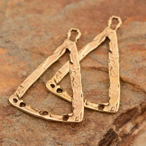 May include: Two bronze-colored, textured metal earring components. Each component is a stylized triangle with a loop at the top and several small holes along the bottom edge. The earrings have a hammered appearance.