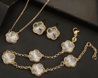 May include: A gold-tone jewelry set with a necklace, bracelet, and earrings. Each piece features a delicate, clear clover-shaped pendant with a textured design.