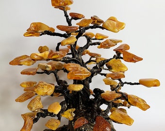 May include: A decorative amber tree sculpture. The tree features a dark, textured trunk and branches, with numerous amber-colored stones resembling leaves. The sculpture is set on a dark, rectangular base.