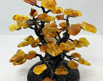 May include: A small amber tree sculpture with a black metal base and a black marble base. The amber pieces are arranged in a tree shape with branches and leaves.