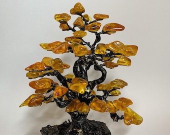 May include: A small amber tree sculpture with a black wire frame and a black base. The amber pieces are shaped like leaves and are arranged in a tree-like pattern.
