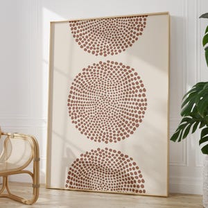 May include: A rectangular wall art print featuring three vertically aligned circular shapes composed of numerous small, dark terracotta-coloured dots against a solid, light beige background, all enclosed within a thin, light-toned wooden frame.