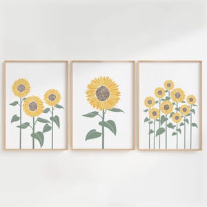 K&ouml;nnte beinhalten: Ein Set aus drei gerahmten Wandbildern mit Sonnenblumen-Illustrationen. Das linke Bild zeigt drei Sonnenblumen, das mittlere eine gro&szlig;e Sonnenblume und das rechte acht Sonnenblumen, alle mit gelben Bl&uuml;tenbl&auml;ttern und gr&uuml;nen St&auml;ngeln.