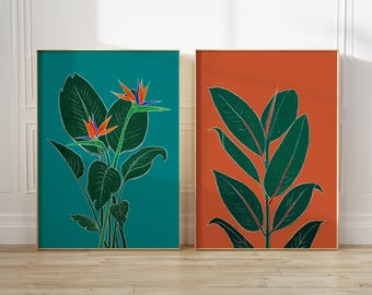 May include: Two rectangular wall art prints. The left print features a bird of paradise plant with dark green leaves and orange and blue flowers on a teal background. The right print displays a rubber plant with dark green leaves on an orange background.
