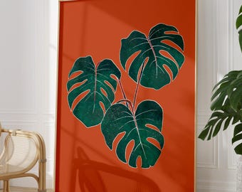 May include: A rectangular wall art print featuring three dark green monstera leaves with visible white vein outlines, set against a solid burnt orange background. The artwork is encased in a thin, light-colored wooden frame.