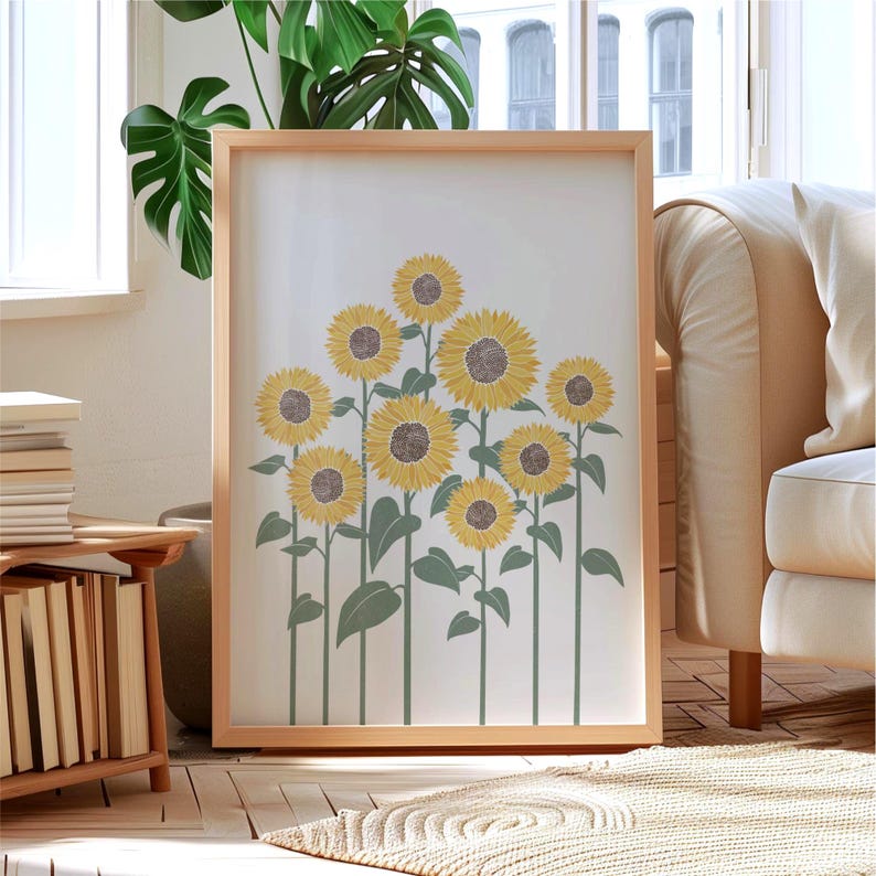 K&ouml;nnte beinhalten: Ein gerahmter Kunstdruck mit einer Ansammlung gelber Sonnenblumen mit braunen Mitten sowie gedeckten gr&uuml;nen Stielen und Bl&auml;ttern. Die Illustration befindet sich auf einem schlichten wei&szlig;en Hintergrund und ist in einem hellen Holzrahmen gefasst.