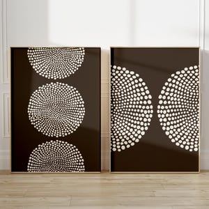 Peut inclure: Deux impressions d'art abstrait encadrées. L'une présente trois cercles pointillés blancs sur fond marron foncé. L'autre montre deux demi-cercles pointillés blancs sur fond marron foncé. Les deux sont dans des cadres dorés.