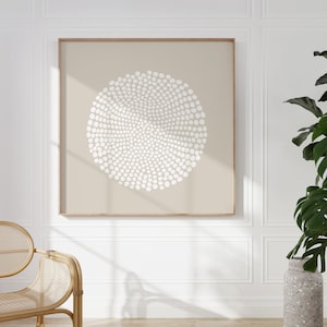 May include: A beige framed print featuring a white abstract design of a circle made of small dots. The design is centred on a beige background.