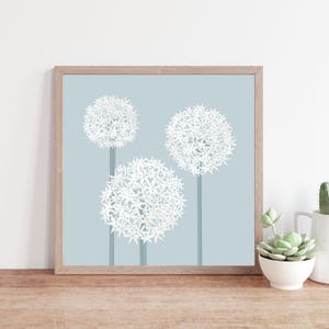 May include: A framed print of three white, round, flower-like plants on a light blue background. The plants have a starburst pattern.