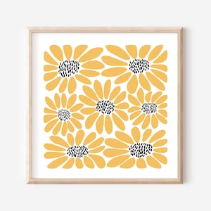 May include: A framed print with a repeating pattern of stylized yellow flowers with black centres on a white background. The flowers have rounded petals and are arranged in a grid. The frame is a light wood colour.